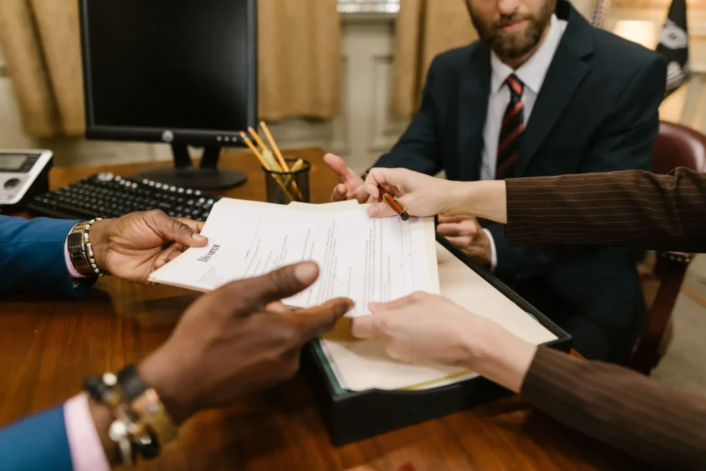 Vender precatório penhorado: Reunião em escritório com advogados assinando documentos em mesa de madeira, com papéis e canetas ao centro, ambiente corporativo e formal.